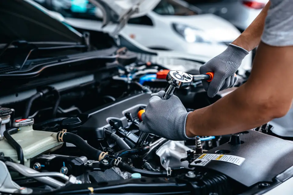 Mechanic wearing gloves tightening a bolt in a car engine under the hood, close-up view of the work.