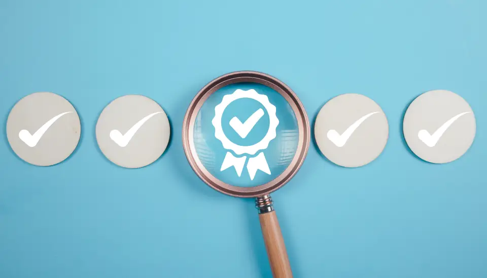 Magnifying glass highlighting a blue certification badge with a checkmark, flanked by five check-mark circles on a blue background.