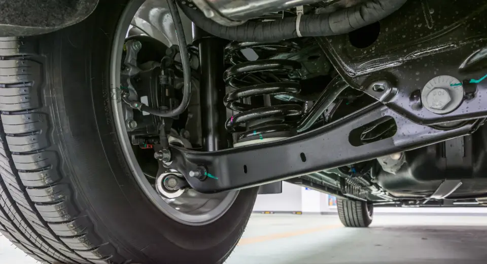 Underside view of a car's front suspension with a coil spring, control arms, and tire visible from below.